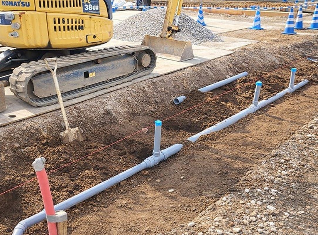 建設現場にて重機を使用して進められる排水管の配管工事