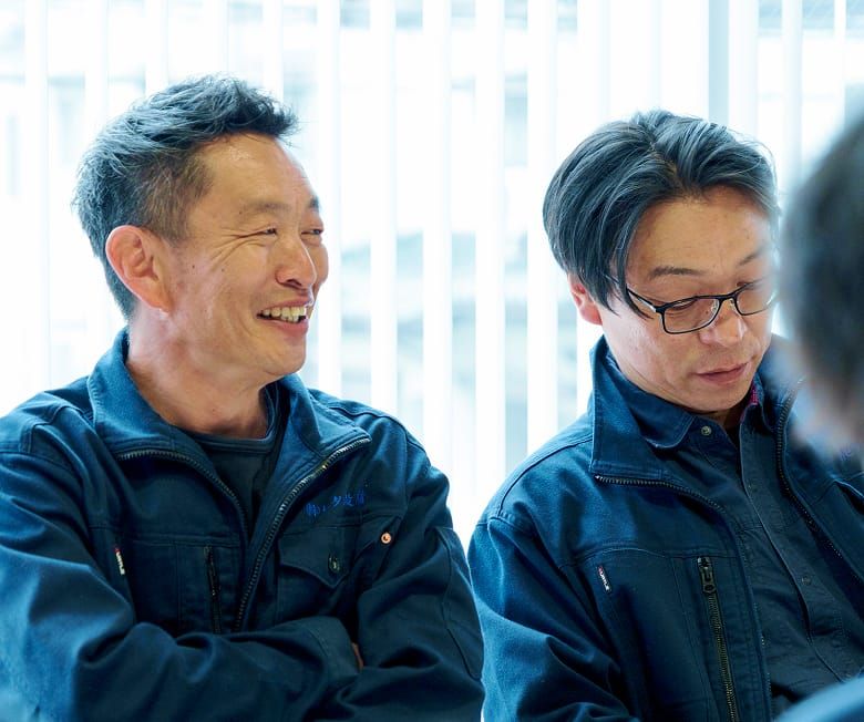 株式会社ヒタチ設備の作業服を着用したスタッフが、笑顔で談笑している社内の和やかな雰囲気。
