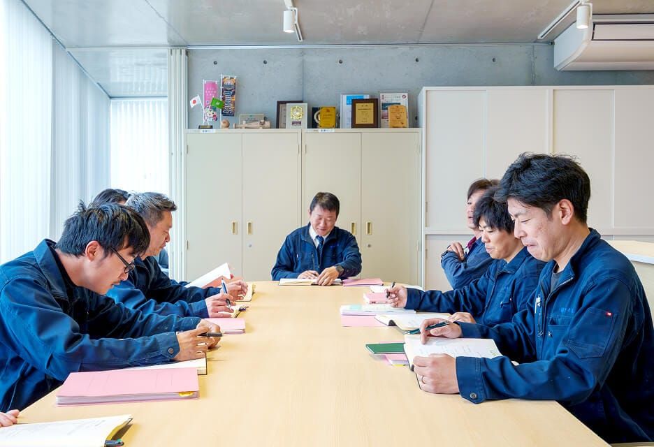 会議室にて作業服を着用した社員たちが真剣に打ち合わせを行う様子