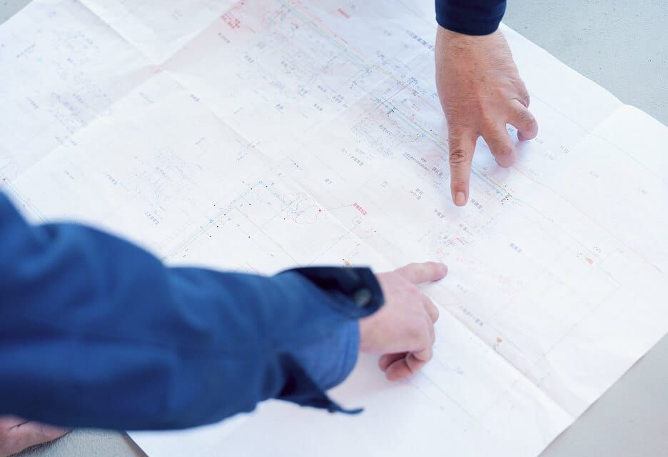施工図面を広げ、現場での作業手順や詳細箇所を指差しで確認する様子