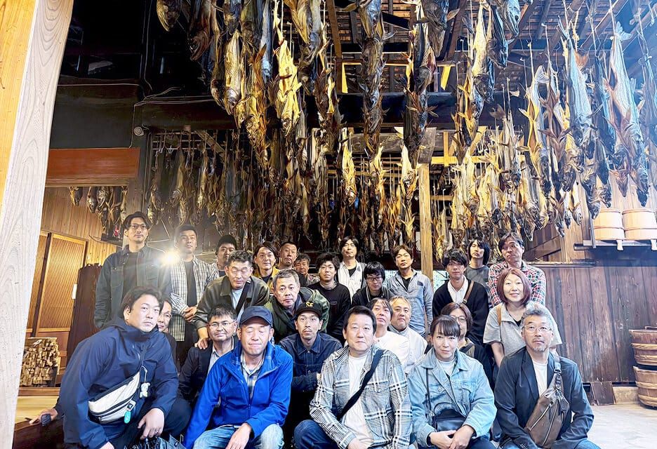 天井に大量に吊るされた鮮を背景に集まった、社員旅行中のヒタチ設備スタッフ一同