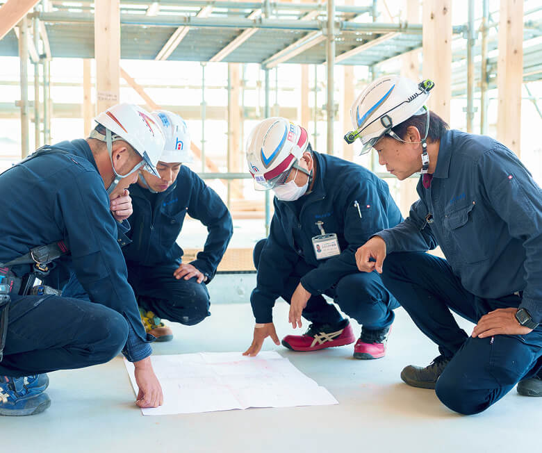 建設現場で図面を囲み、真剣な表情で打ち合わせを行うヒタチ設備のスタッフたち