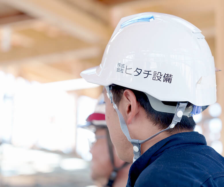 株式会社ヒタチ設備のヘルメットを着用して現場で働くスタッフの横顔