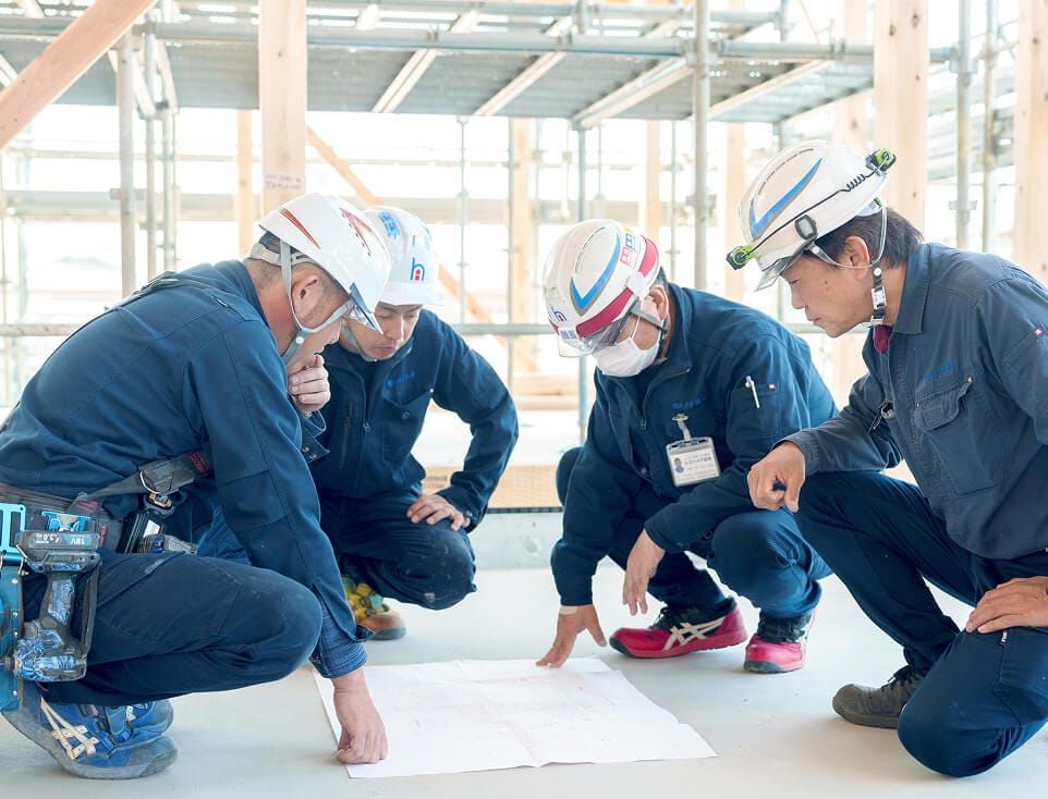 建設現場の床に広げた図面を囲み、真剣な表情で打ち合わせをする4名のスタッフ