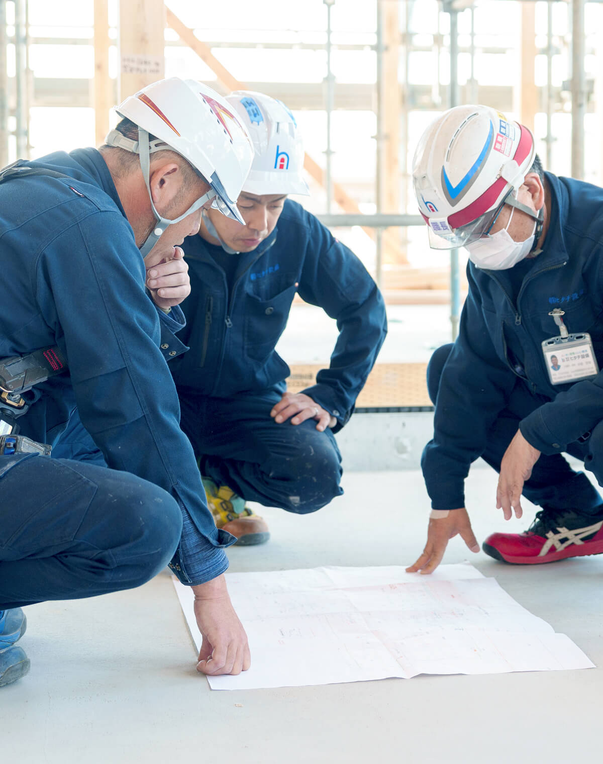 建設現場で図面を囲み、施工の打ち合わせを真剣に行うヒタチ設備の作業員