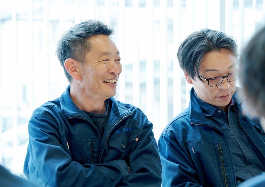 笑顔で談笑する株式会社ヒタチ設備のスタッフ。円滑なコミュニケーションを象徴しています。